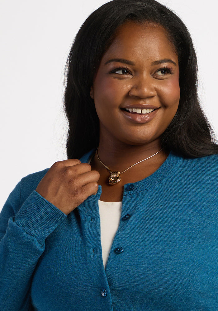 Woman smiling, wearing the Woolx Caitlin Sweater in Blue Pine over a white shirt, holding her cardigan with one hand.