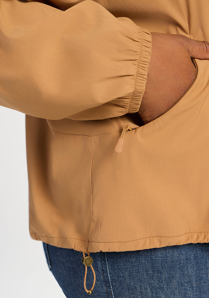 Close-up of a tan, all-season Cooper Windbreaker - Saddleback with a zippered pocket and a drawstring hem.