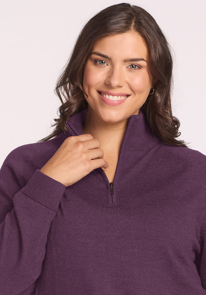 Woman with wavy brown hair smiles in a Woolx Collins Half Zip Sweater - Purple Iris, against a light backdrop.