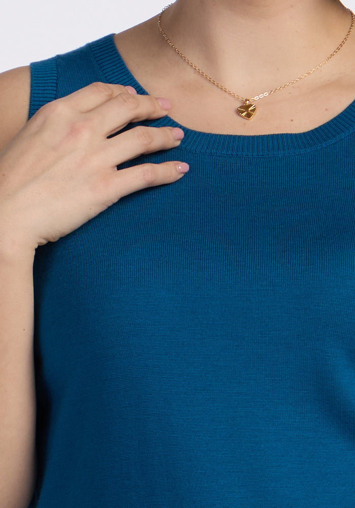 Someone wearing the Woolx Chessy Tank Top in Moroccan Blue touches their collarbone. They have short, light pink manicured nails and sport a gold necklace with a heart-shaped pendant.