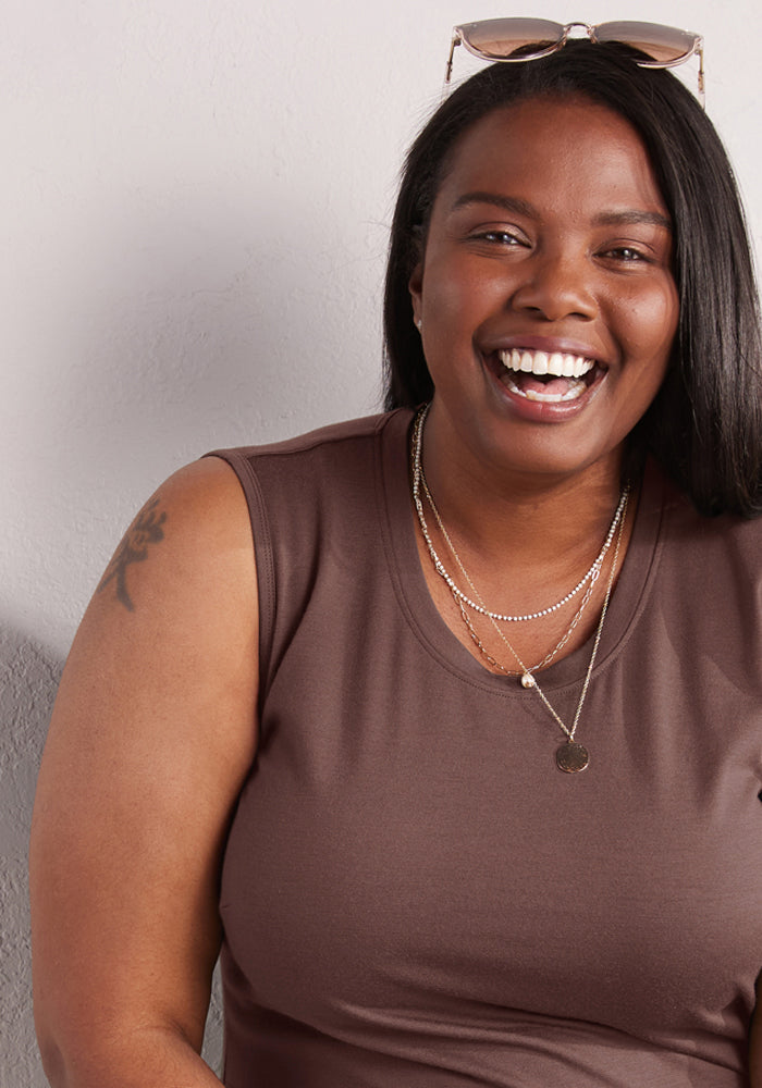 A smiling woman wears the Woolx Cassie Dress in Peppercorn, layered necklaces, and sunglasses on her head.