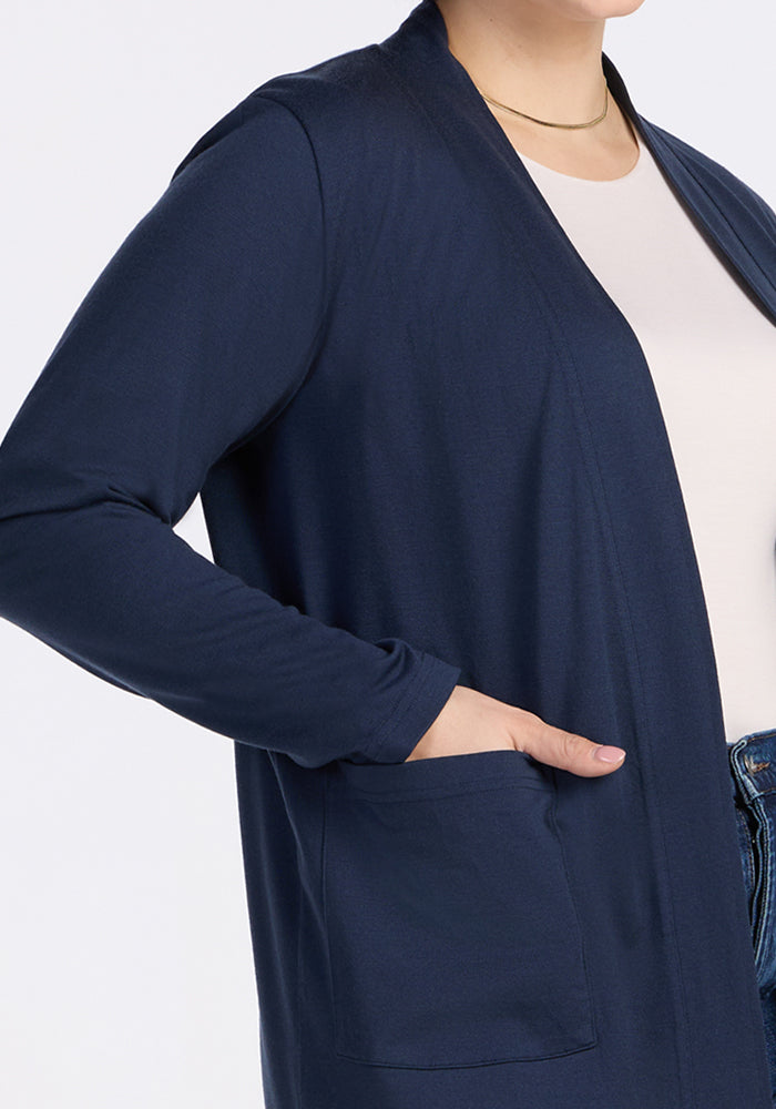 A person in a Woolx Paisley Cardigan - Deep Navy, layered over a white shirt and blue jeans, stands with one hand in the cardigan pocket. Their head is partially out of frame.