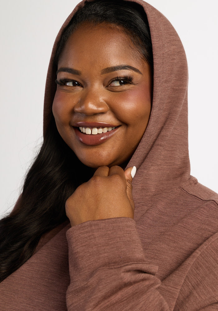 A smiling woman wearing a brown moisture-wicking Woolx Genevieve Hoodie - Sable Heather.