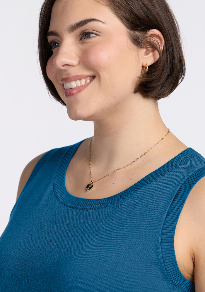 Woman with short brown hair wears a Woolx Chessy Tank Top in Blue Pine and a gold necklace, smiling to the side.