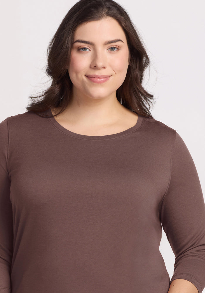 A woman with wavy brown hair smiles softly, wearing the Woolx Jenny 3/4 Sleeve Crew Neck in Peppercorn.