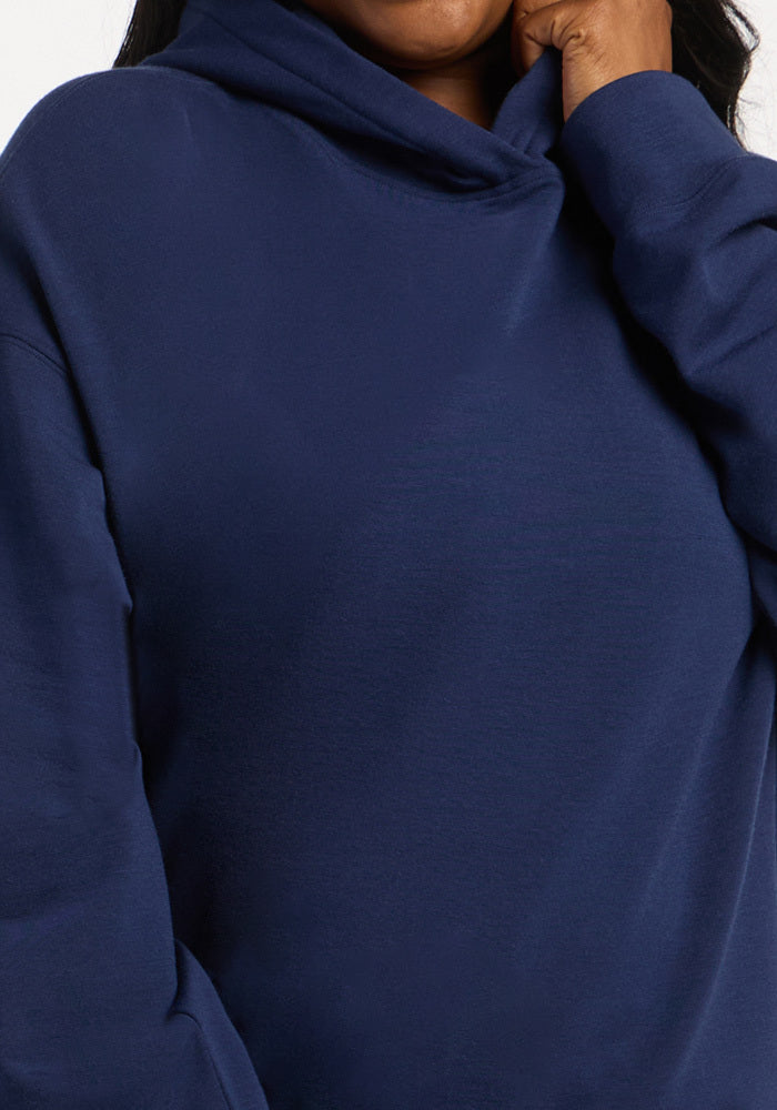 A person wearing a dark blue, moisture-wicking, temperature-regulating Woolx Genevieve Hoodie in Ocean Cavern.
