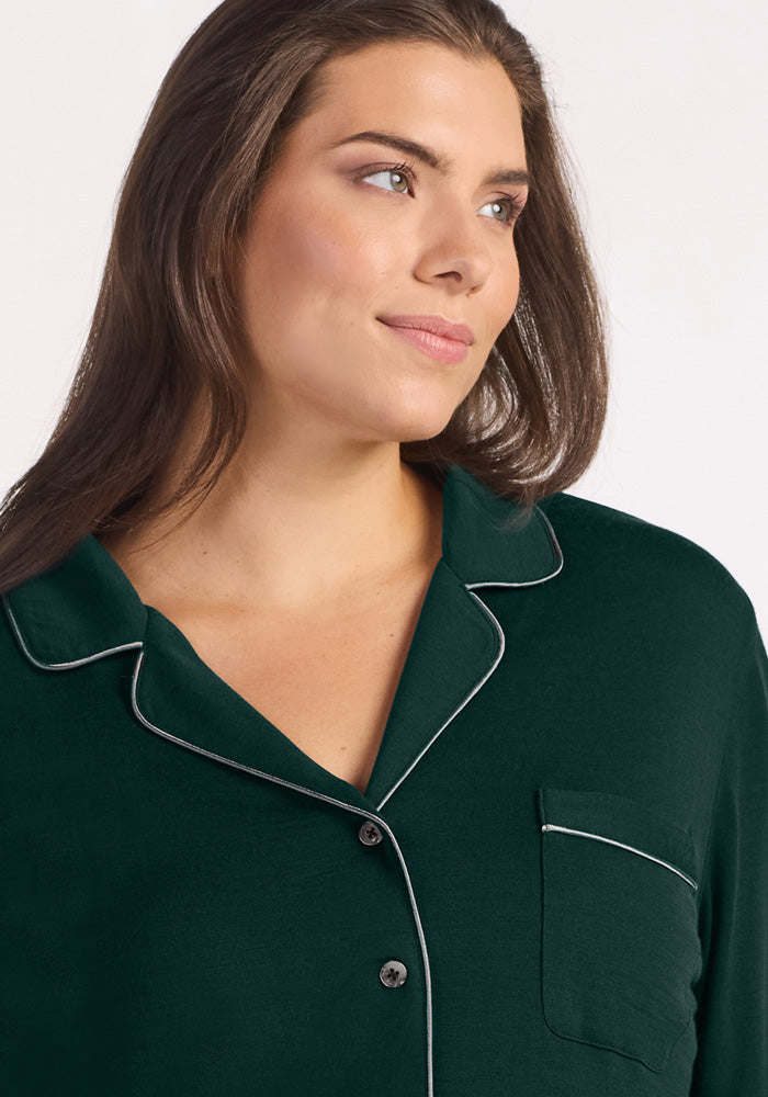 A woman wearing a deep pine Harper FeatherTouch® Pajama Set top with light-colored piping and a chest pocket.