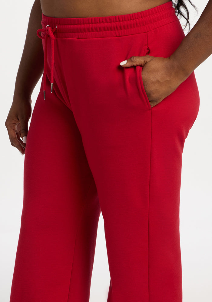 Model wears Woolx Eloise Wide Leg Pants in Maraschino Cherry, hand in pocket, white background, torso cropped.