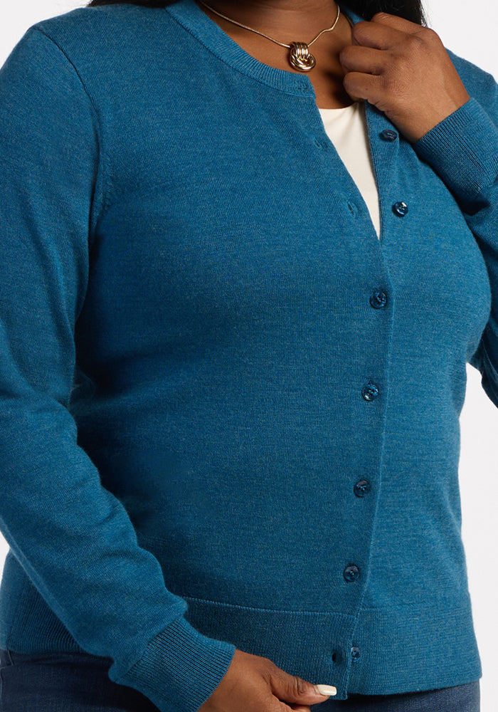 Person wears Woolx Caitlin Sweater - Blue Pine over a white shirt, holding the collar and hem of the cardigan.