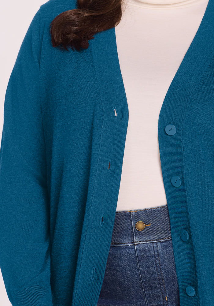 Person wearing a Woolx Gia Sweater - Blue Pine over a white turtleneck and high-waisted blue jeans.