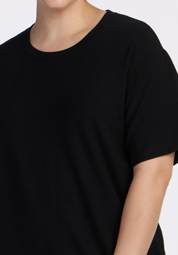 A person wearing the Woolx Audrey Tee in black, a relaxed fit short-sleeve T-shirt, is shown from shoulders to hips against a neutral background.