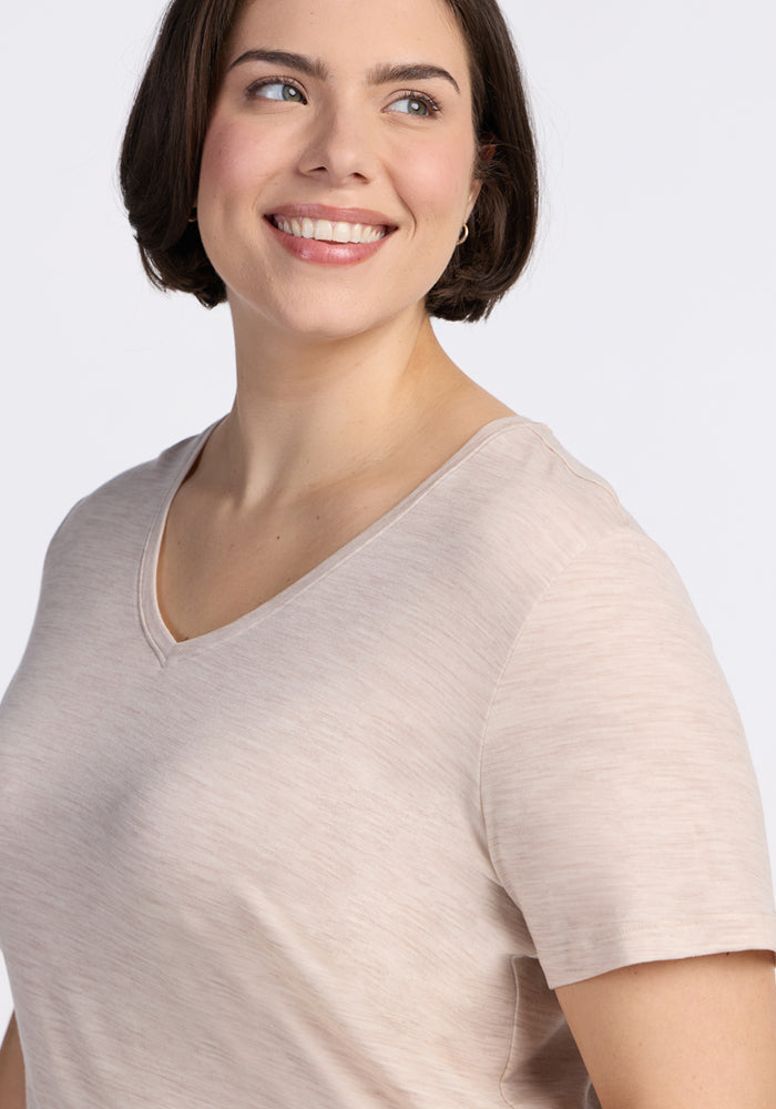 A woman with short brown hair, wearing the Woolx Junie V Neck in Cream Heather, smiles while looking slightly to her left against a plain white background.