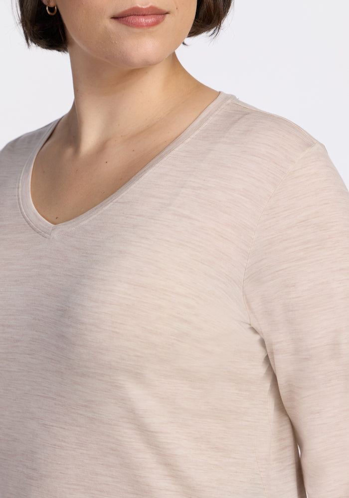 A person with short brown hair models the Woolx Millie Long Sleeve in Cream Heather, a V-neck Merino wool top, shown from shoulders to mouth against a plain background—ideal for temperature-regulating comfort.