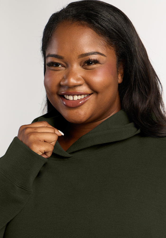 Smiling woman wearing a dark green Genevieve Hoodie - Duffel Bag made of merino wool.