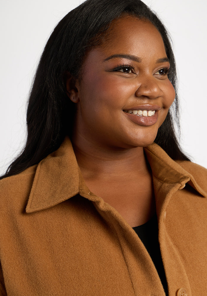 Smiling woman in the Woolx Jovie Shacket - Saddleback, perfect for cozy layering against a plain background.