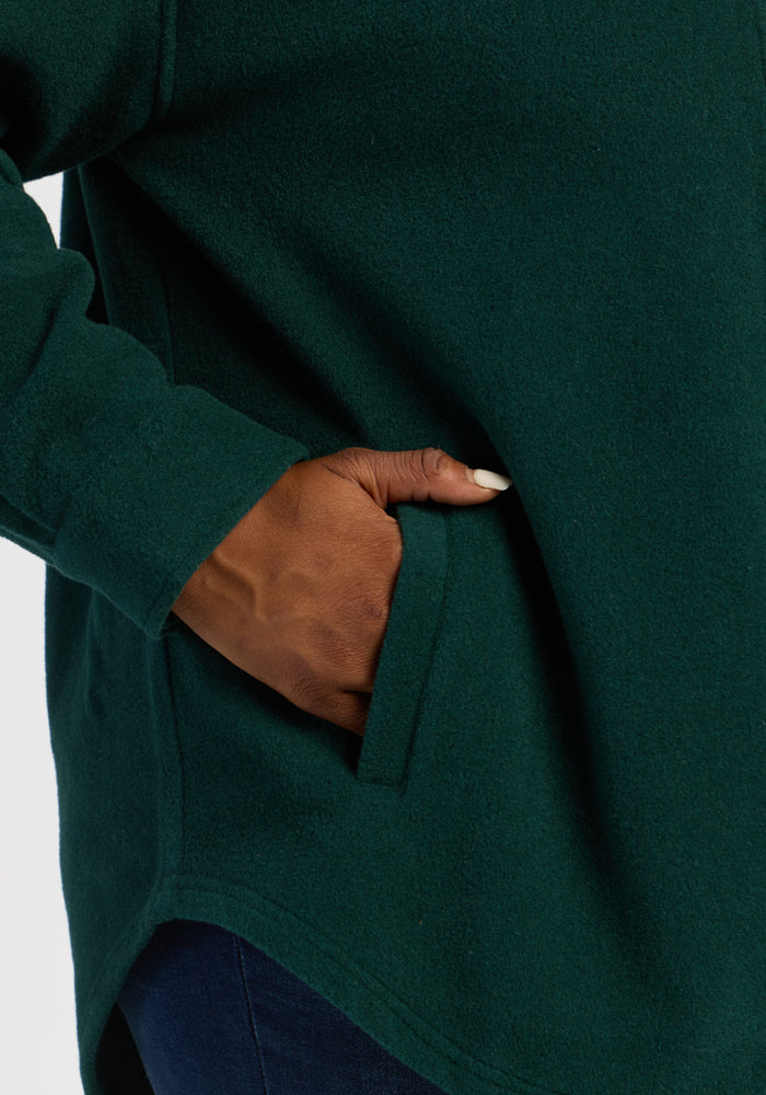 A hand rests in the pocket of a Woolx Jovie Shacket - Deep Pine, a cozy layer perfect for cool days.