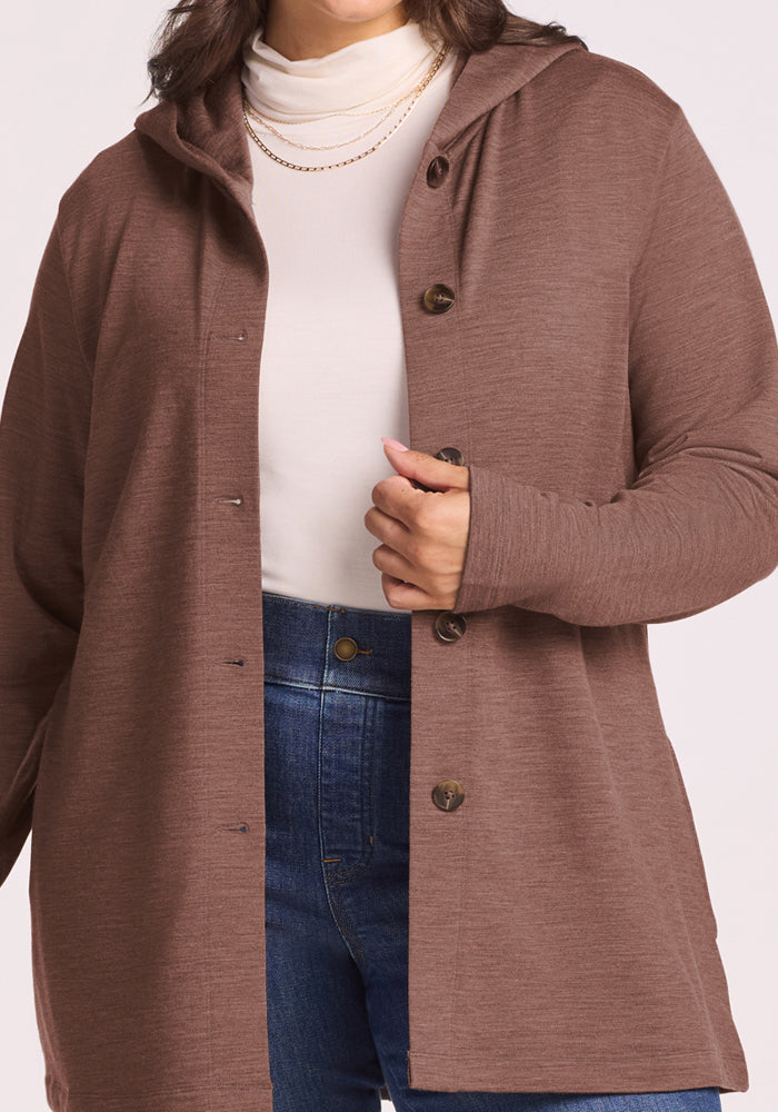 Woman in Woolx Edna Hooded Cardigan in Sable Heather, layered over a white turtleneck and blue jeans.