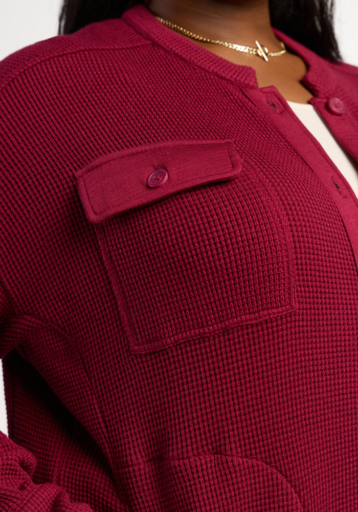 Close-up of someone in the Woolx Oaklynn Waffle Shacket in Beet Red, featuring a front pocket and gold necklace.