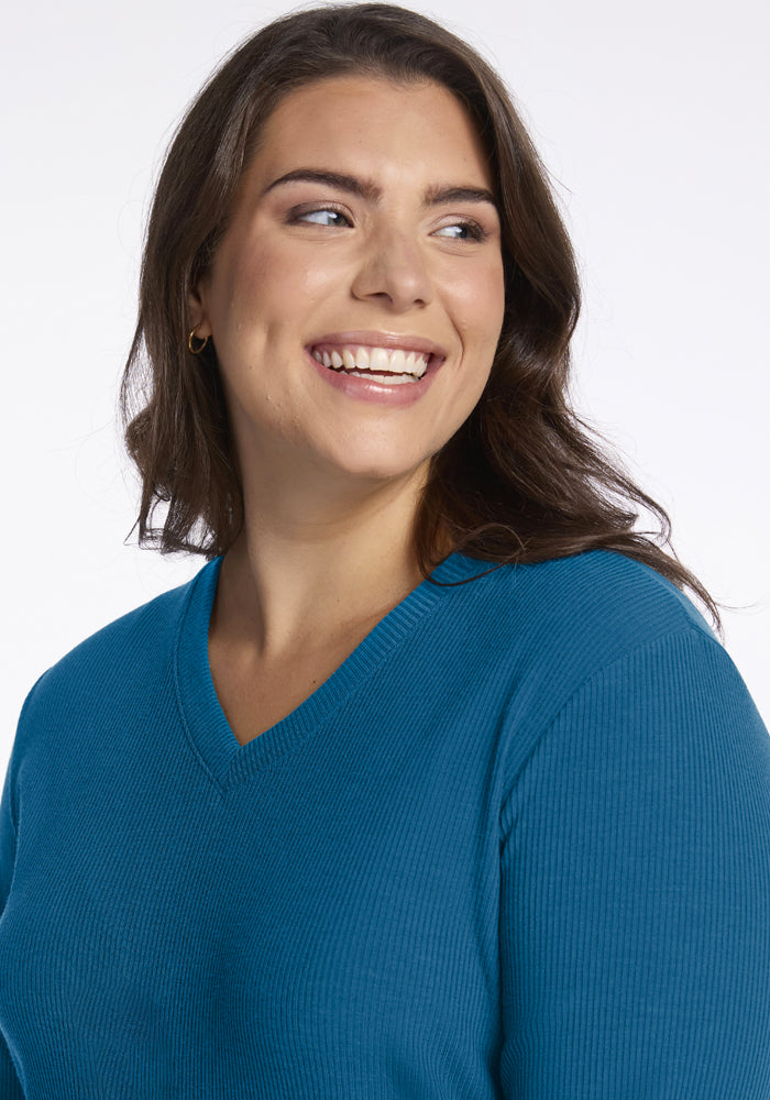 Smiling woman with brown hair in Woolx Evie Ribbed Tunic - Blue Pine, looking left, on white background.