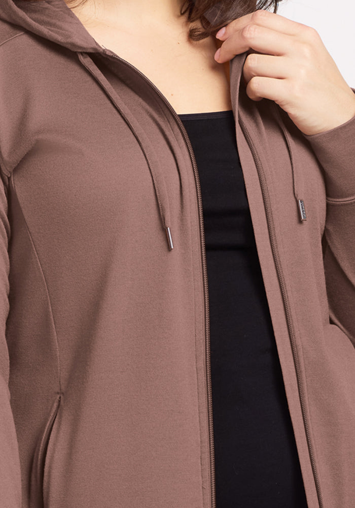 A person wears the Woolx Ryann Hoodie in Toasted Almond over a black top—it's the perfect travel essential.