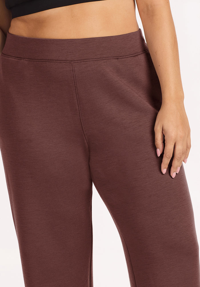 A person wears Woolx Bree Lounge Pants in Canyon Clay and a black crop top, with one hand resting by their side.