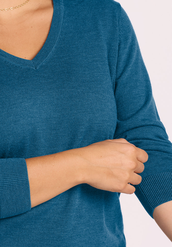 Person in a Woolx Francesca Sweater - Blue Pine, adjusting the sleeve with their right hand.