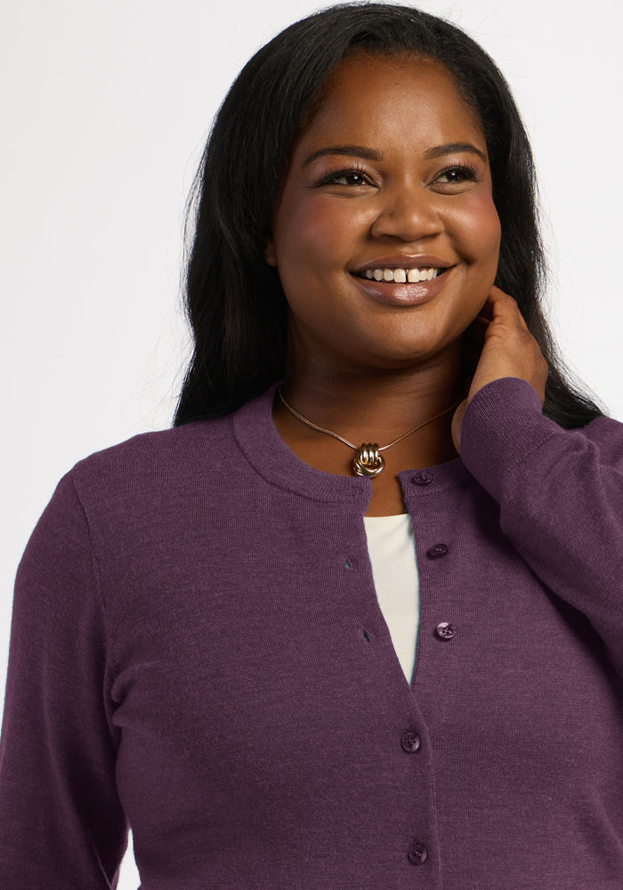 Smiling woman in the Woolx Caitlin Sweater - Purple Iris, white top, and necklace, touching her hair.