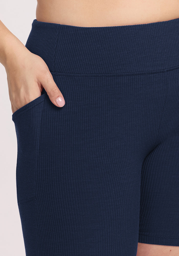 A close-up of a person wearing Woolx Miley Bike Shorts in Deep Navy, featuring ribbed fabric, a wide waistband, and a fitted, comfortable style with their right hand resting in the pocket.