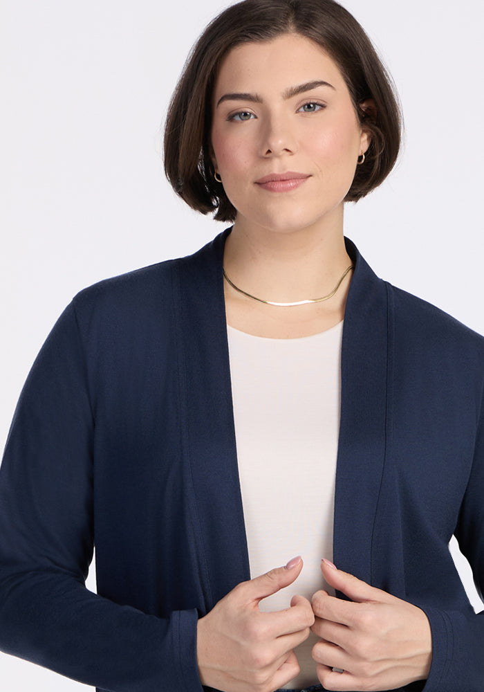 A woman with short brown hair wears the Woolx Paisley Cardigan in Deep Navy over a light top, accessorized with a gold necklace and small hoop earrings. She has a neutral expression and holds the edges of her women's cardigan.