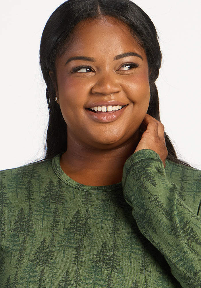 Woman smiling in Woolx Maddie Baselayer Top - Forest Friends, touching her neck against a white background.