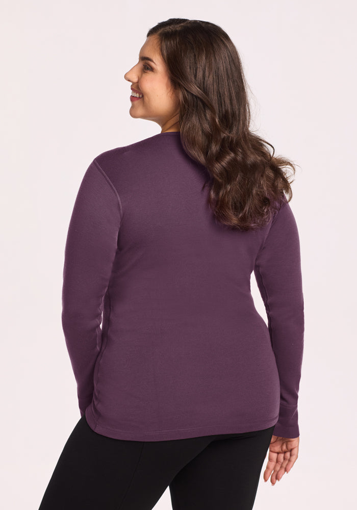 Woman with wavy brown hair in a Woolx Hannah Long Sleeve Top - Purple Iris and black pants, smiling.