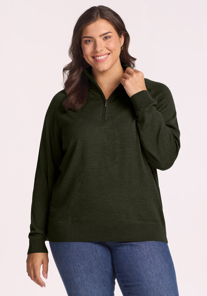 Woman in Woolx Collins Half Zip Sweater - Duffel Bag, blue jeans, standing against a light background. 