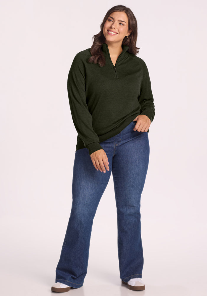 Woman smiles in the Woolx Collins Half Zip Sweater - Duffel Bag, paired with blue jeans against a plain background.