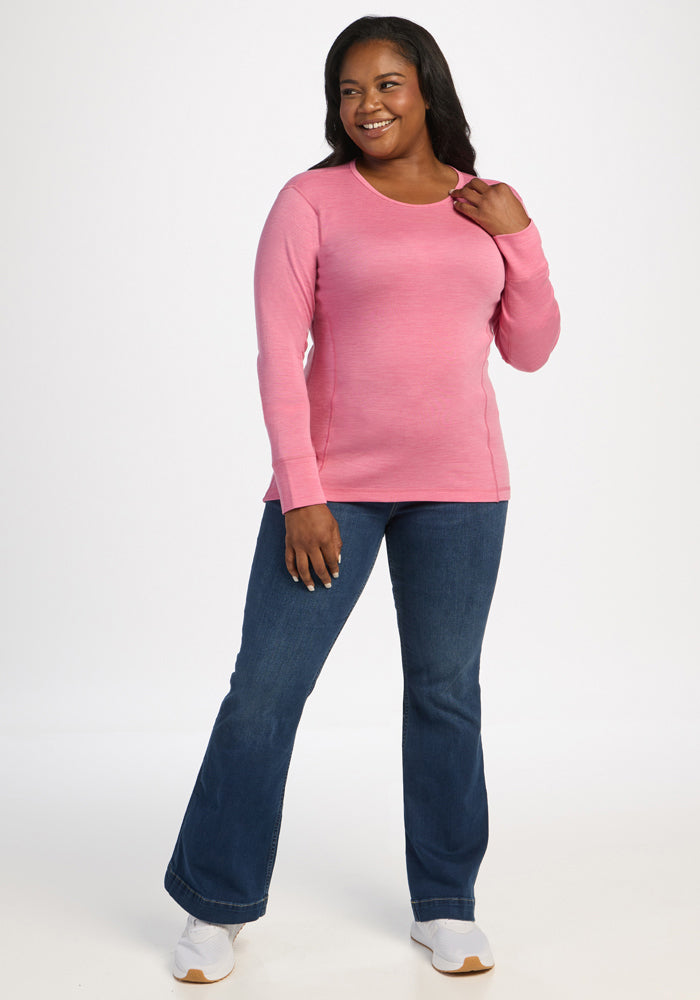 Woman in Woolx Hannah Long Sleeve Top - Pinky Promise, blue jeans & white sneakers smiles against a plain background.
