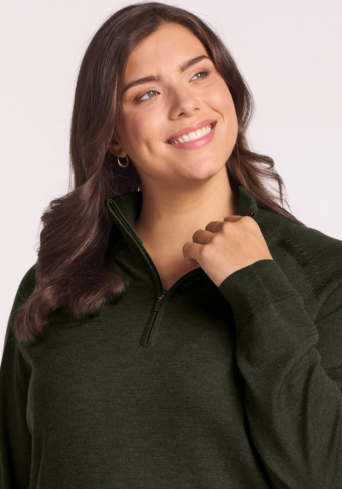 Woman in a Woolx Collins Half Zip Sweater in Duffel Bag smiles and looks upward against a light background.