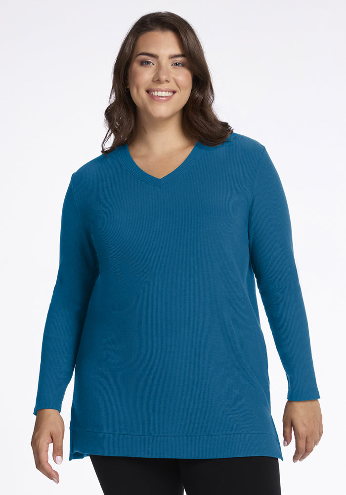Woman in a Woolx Evie Ribbed Tunic - Blue Pine and black pants smiles warmly before a plain white background. 