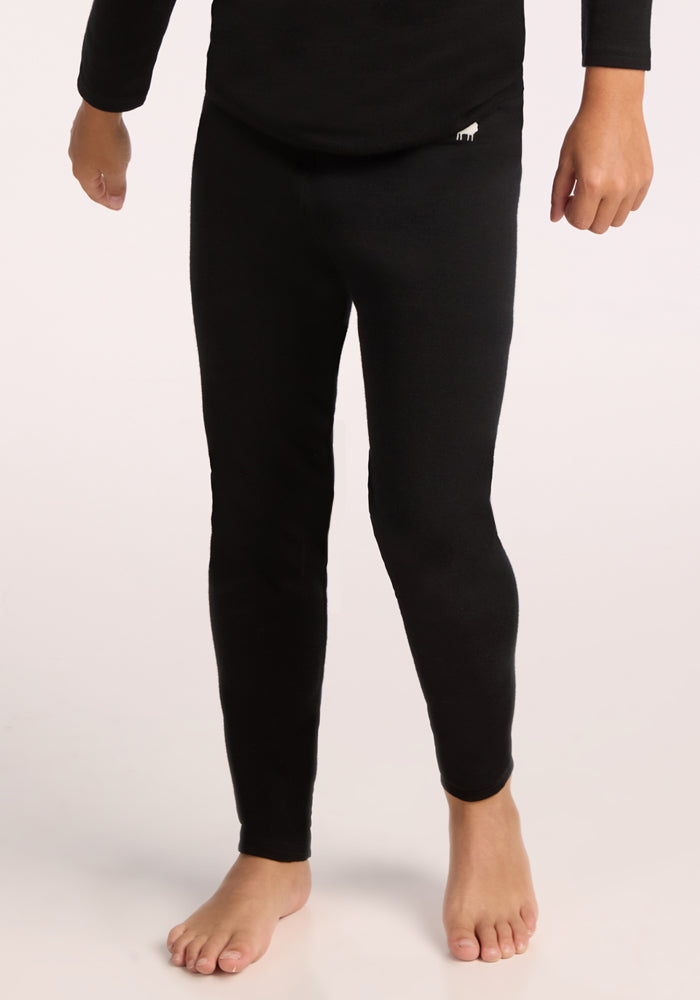A person stands barefoot in black fitted leggings, shown from shoulders to feet against a plain light background—perfect for highlighting Woolx Kids Explorer Base Layer Bottoms - Black. 