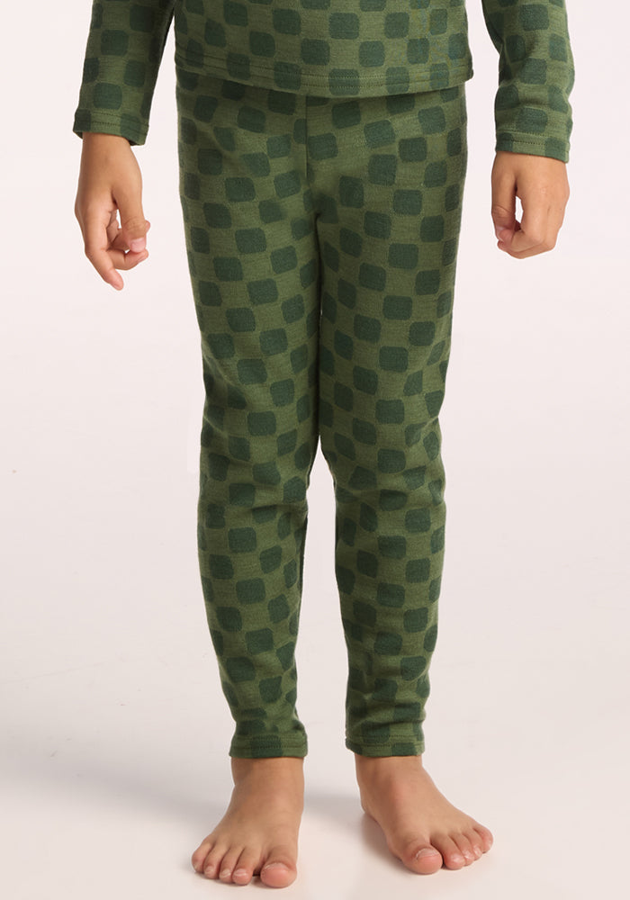 A child stands barefoot, wearing Woolx Kids Explorer Base Layer Bottoms - Frog Hop and a matching long-sleeve top with a dark green checkered pattern; only the body from shoulders down is visible. 