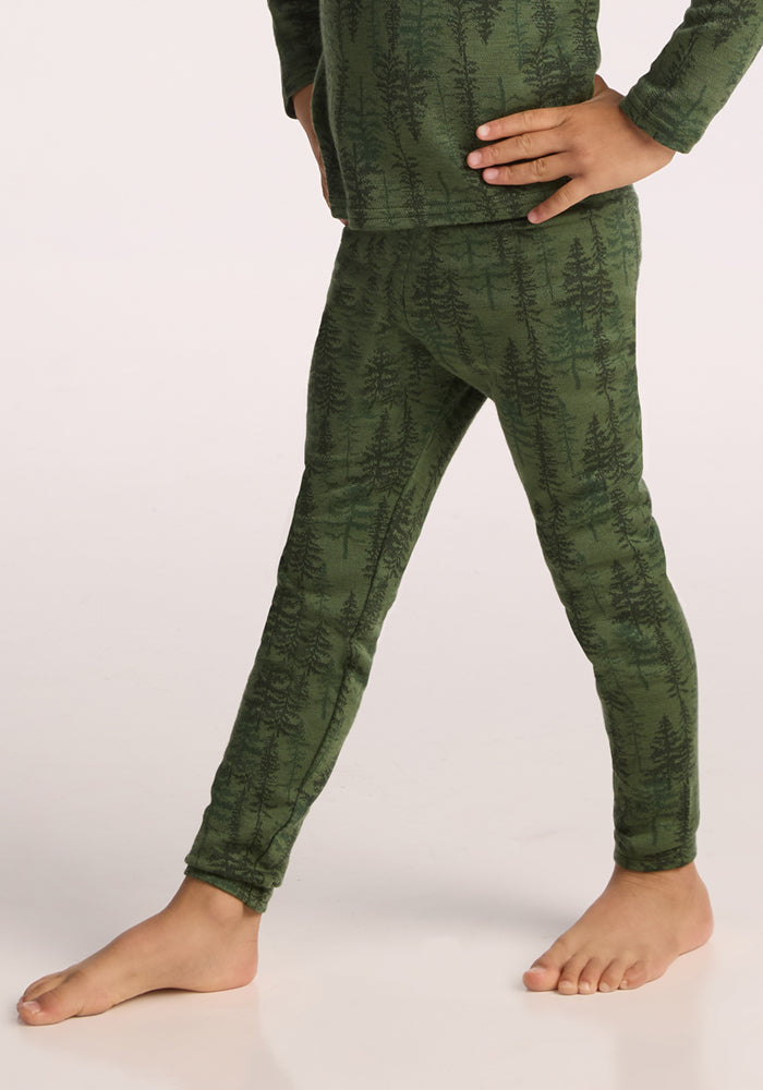 A child models Woolx Kids Explorer Base Layer Bottoms - Forest Friends, standing barefoot on a light surface with one hand on their hip and one leg crossed in front of the other.