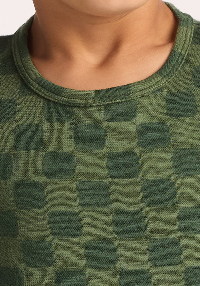Close-up of a child in the Woolx Kids Explorer Base Layer Top - Frog Hop, a green, breathable wool thermal with darker green square patterns and a rounded neckline. Only the child's lower face and neck are visible.