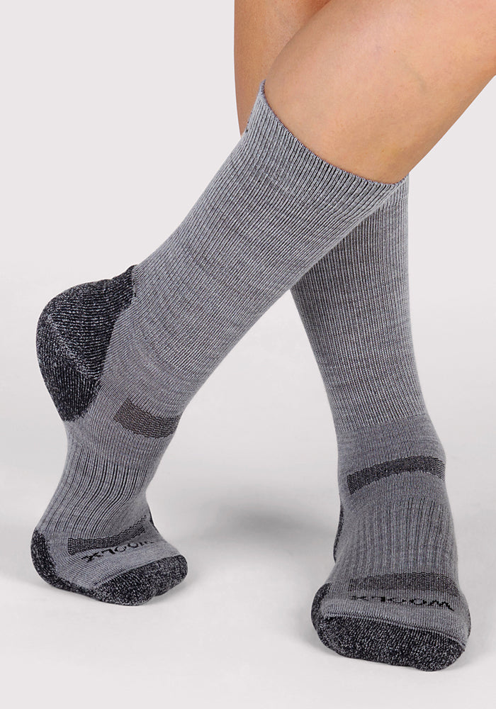 Two feet wear Woolx Womens Harbor Crew Socks in grey, featuring darker gray heels, toes, and accents. The ribbed, breathable Merino wool socks are crossed at the ankles against a plain background.