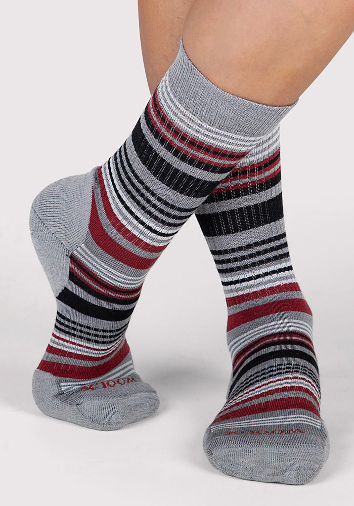 A pair of crossed feet wear Woolx Womens Everyday Crew Socks in Light Grey Stripe—odor-resistant Merino wool socks featuring red, black, and white stripes—against a plain light gray background.