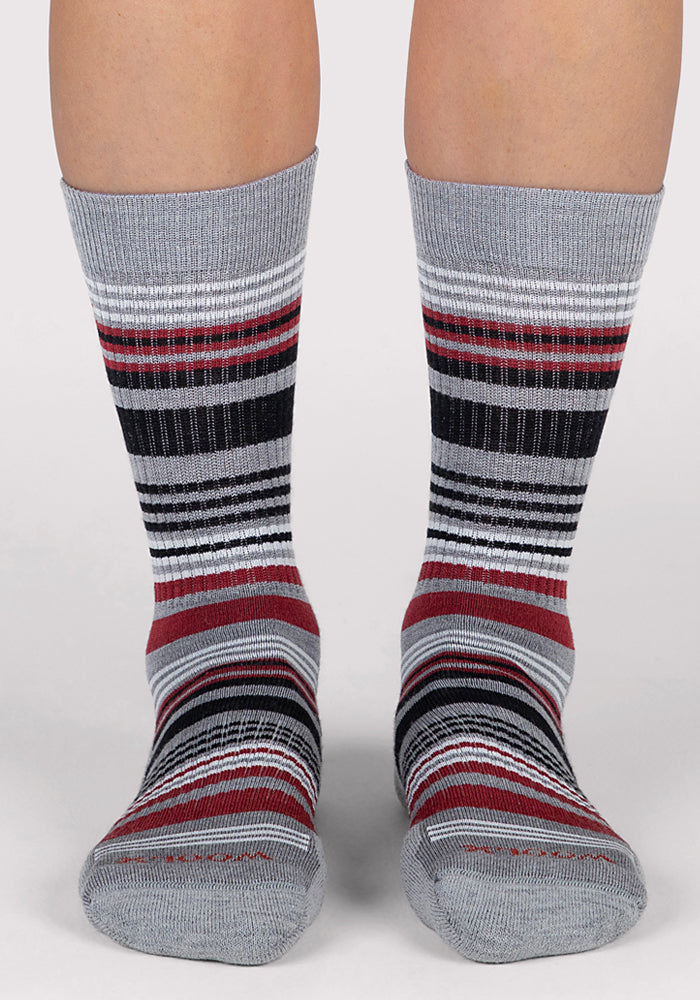 A pair of feet in Woolx Womens Everyday Crew Socks - Light Grey Stripe, featuring horizontal black, white, and red stripes, shown from the front against a light background.