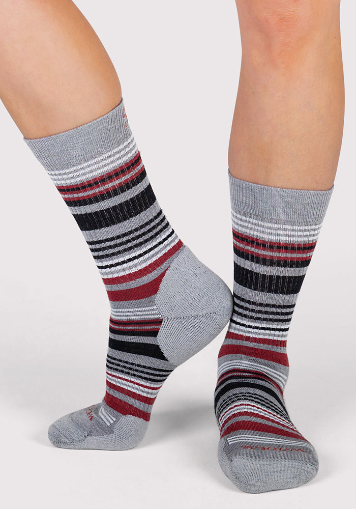 A person wearing Woolx Womens Everyday Crew Socks - Light Grey Stripe stands on a light gray surface, one foot flat and the other slightly raised to show off these odor-resistant Merino wool socks.