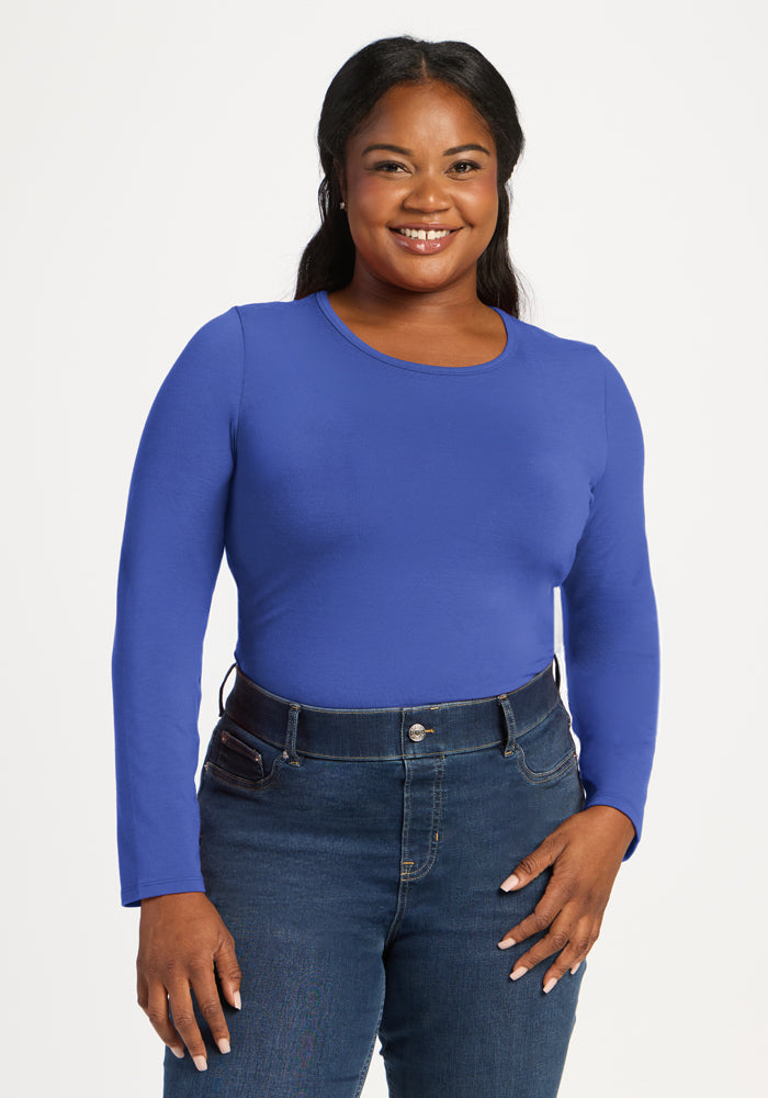 Woman smiles in a Woolx Margot Bodysuit - Royal Blue with jeans, standing against a white background. 