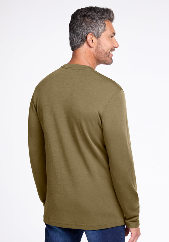 A man with short gray hair stands facing away from the camera, wearing the Woolx Easton Crew Neck Shirt in Winter Moss and blue jeans against a plain light background.