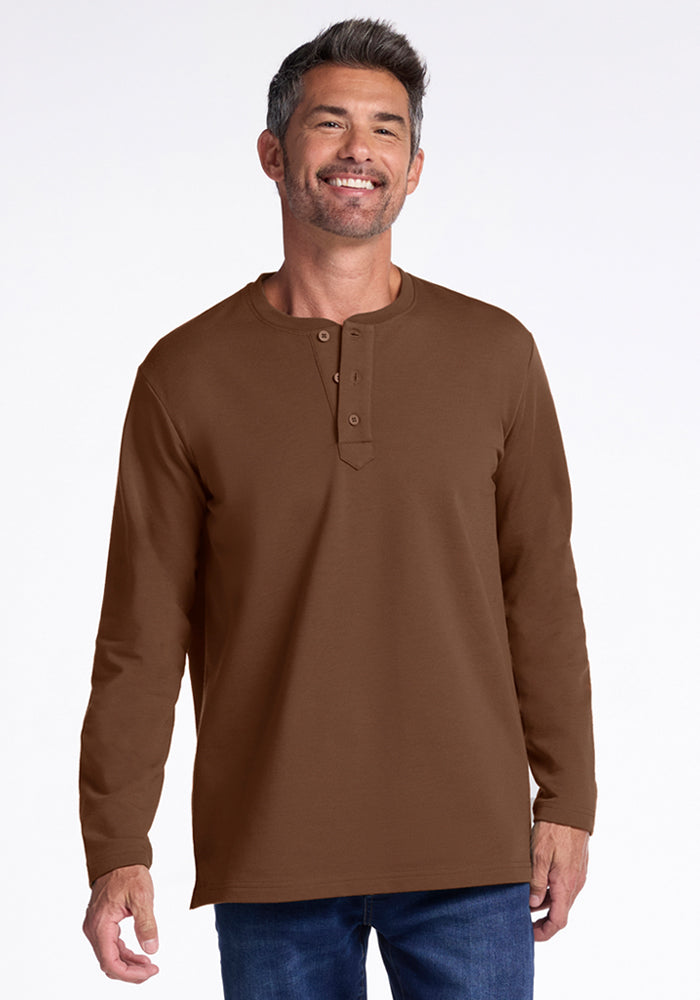A smiling man with short dark hair and some gray, wearing the Woolx Jackson Henley in Bourbon Oak and blue jeans, stands against a plain white background. 