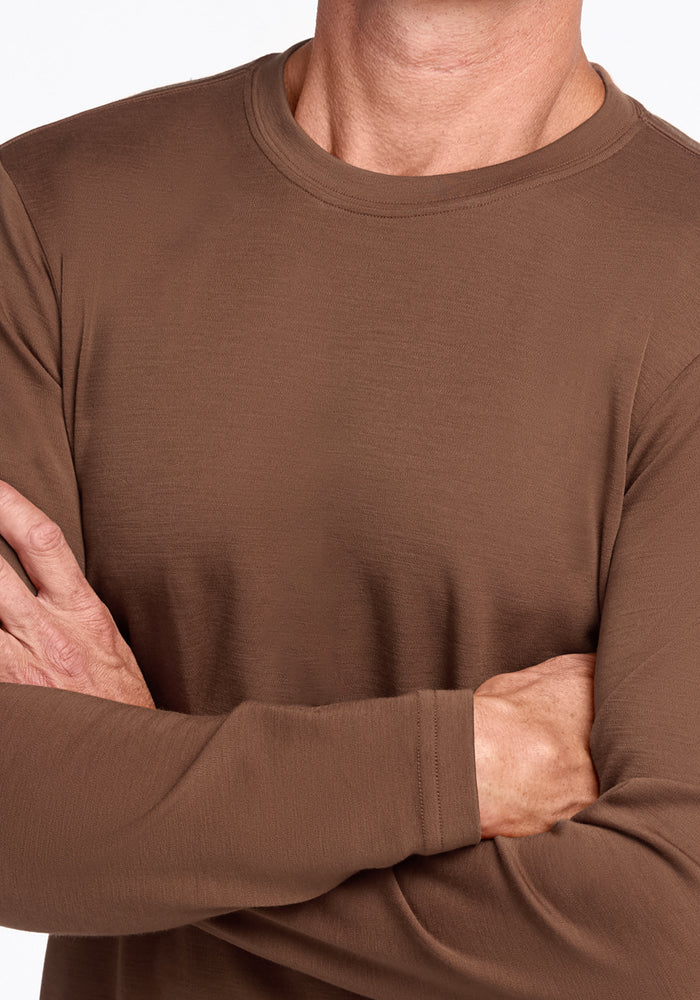 A person wears the Woolx Easton Crew Neck Shirt in Bourbon Oak, arms crossed, shown from the shoulders down against a plain white background.