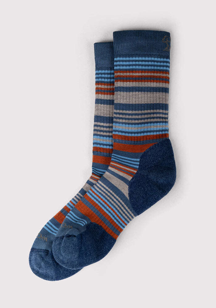 A pair of Woolx Mens Everyday Crew Socks in Majolica Blue Stripe, featuring durable Merino wool with colorful horizontal stripes and solid dark blue heels, toes, and cuffs, are laid flat on a light gray background.