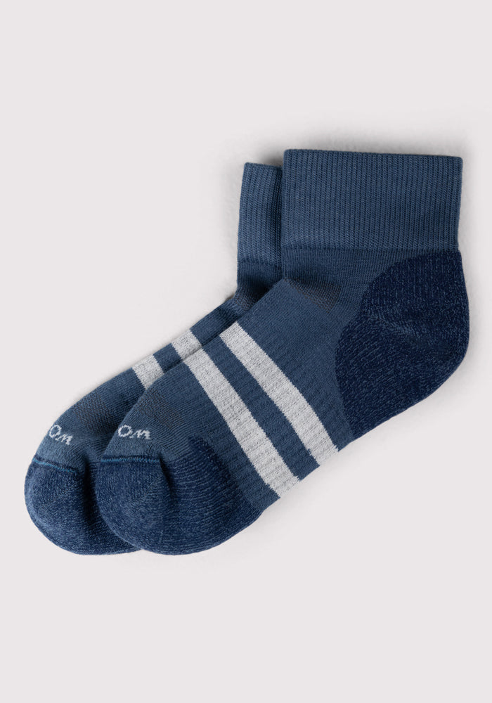 The Woolx Womens Rambler Ankle Sock in Majolica Blue features moisture-wicking fabric, two white stripes, and darker blue heels and toes, shown on a light grey background.